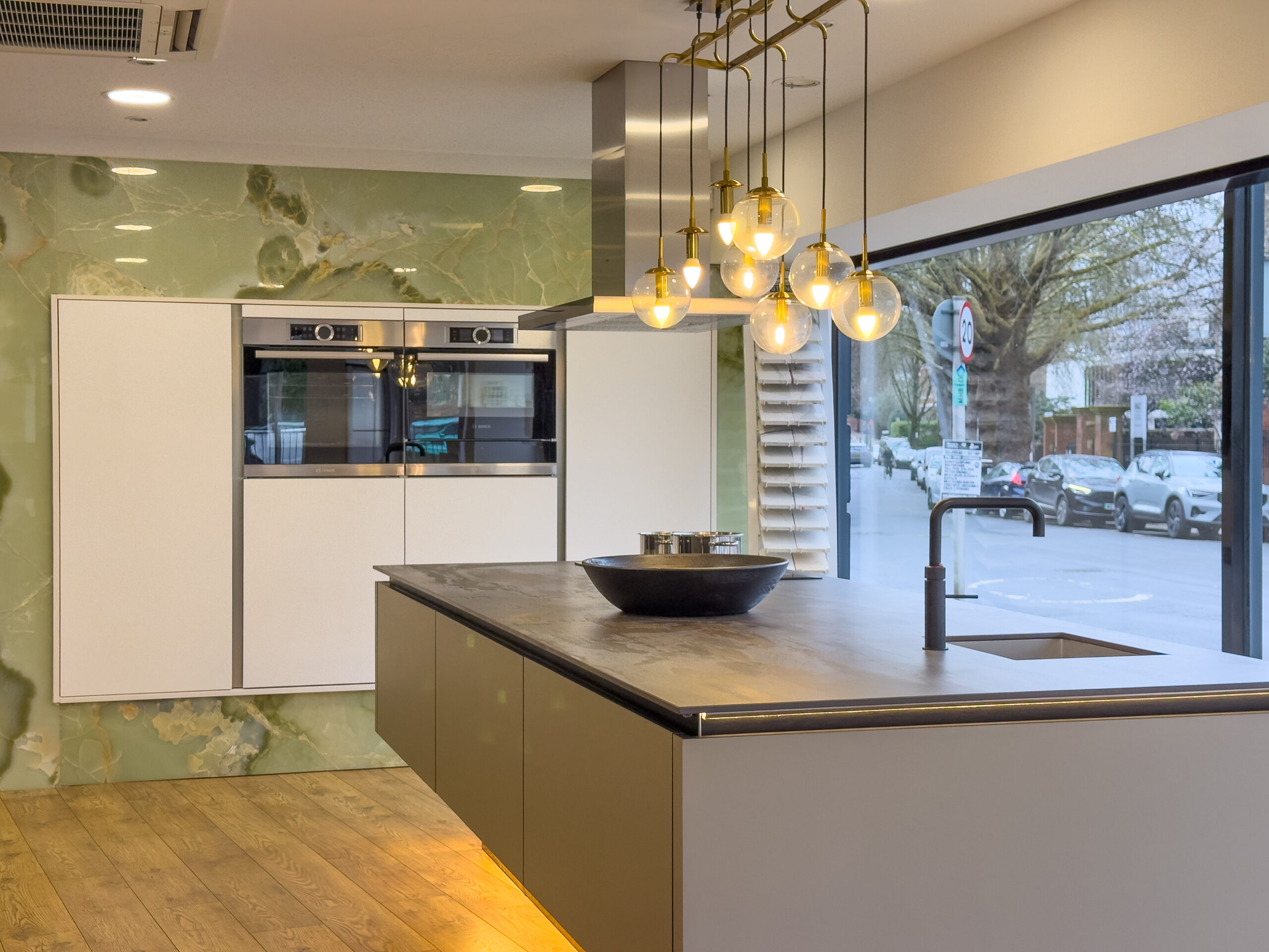gloss kitchen with marble effect feature wall and large island, modern showroom kitchen with statement pendant lights, contemporary kitchen with integrated ovens and window view