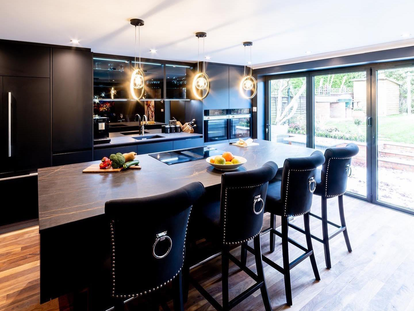 Modern dark kitchen with pendant lights over a large island and sliding garden doors